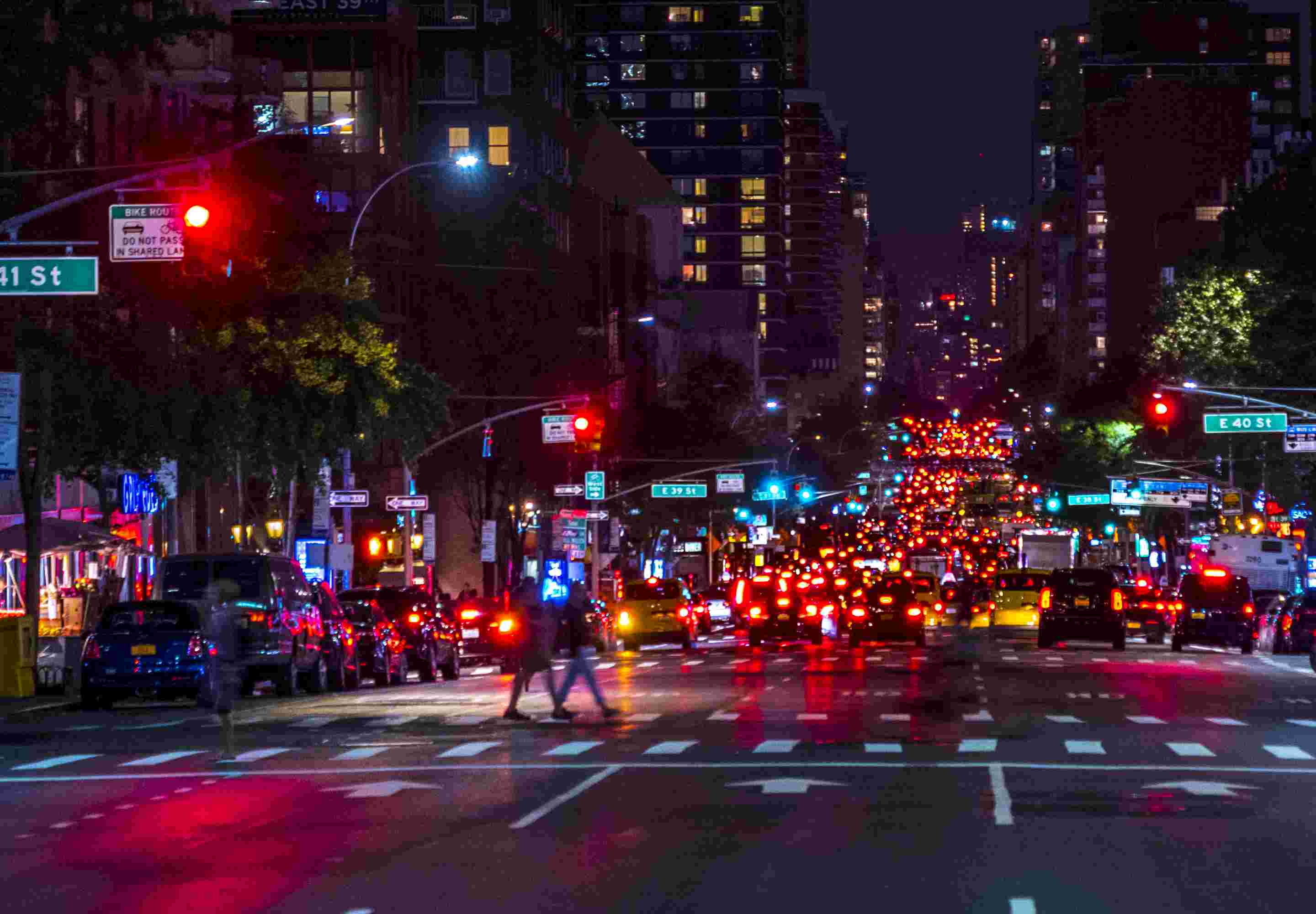 people on pedestrian crossing at night with colorful lights from cars