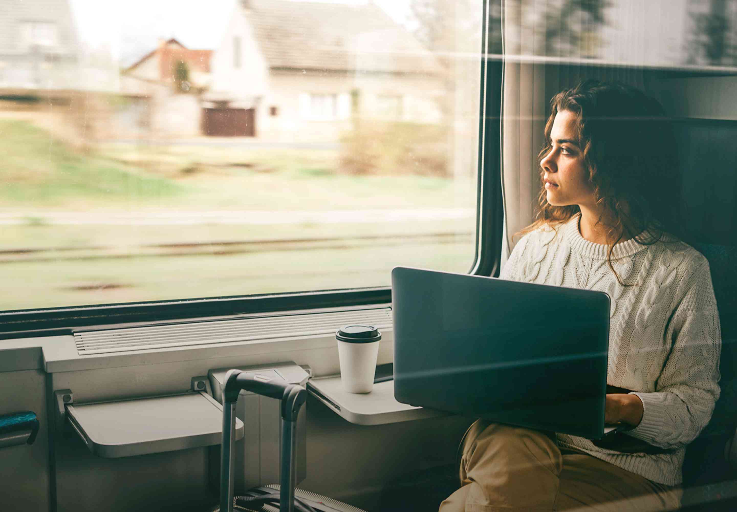 travelling woman looking out window with open laptop on lap