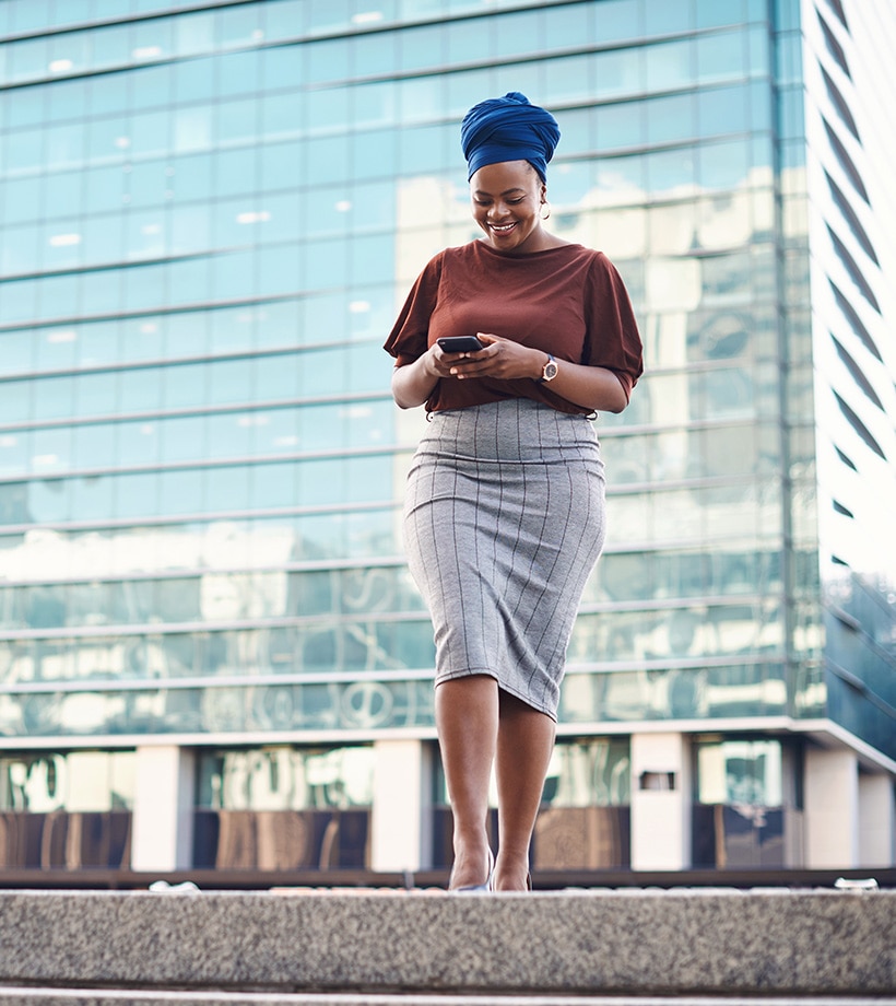 smiling woman walking and looking down at mobile phone in hands