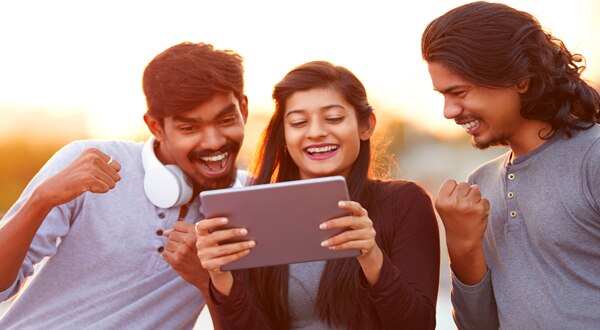Three people standing together laughing at a tablet