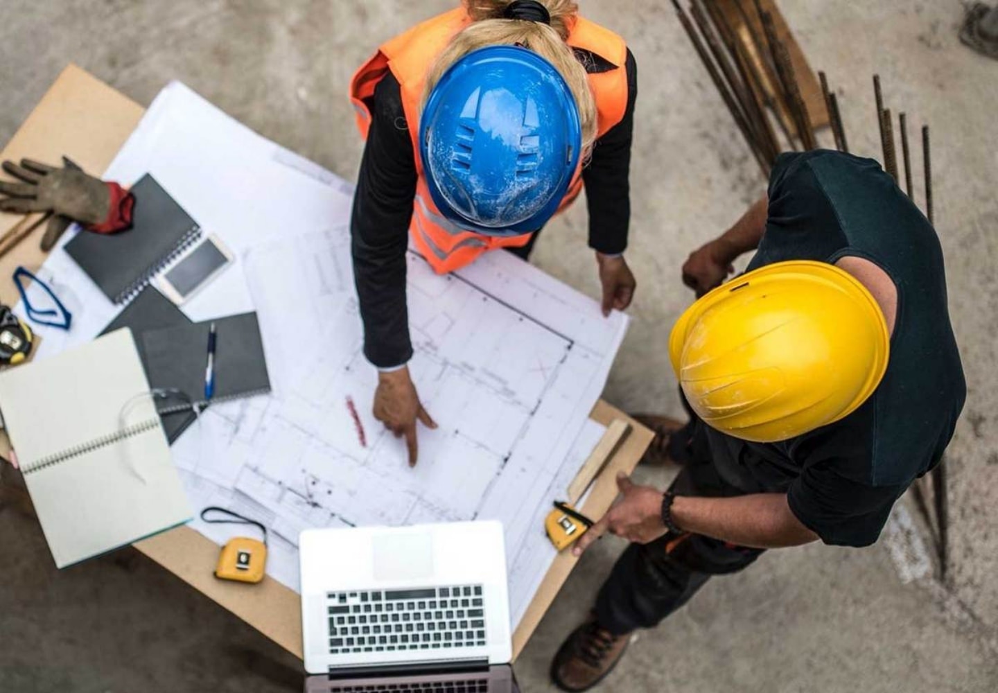 Top view of two people looking construction plan next to a laptop