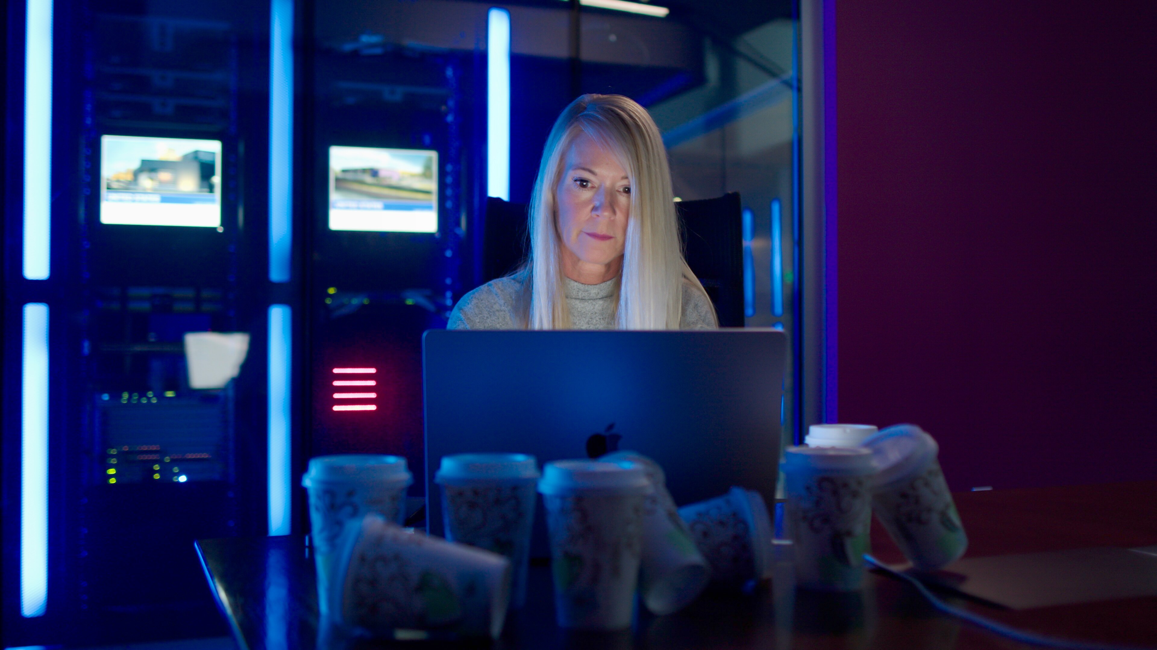 Woman working late at a data center surrounded by empty coffee cups
