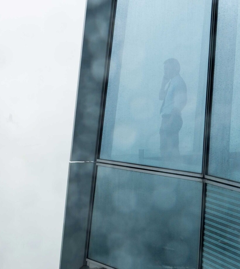 A man looking outside from a tall glass building